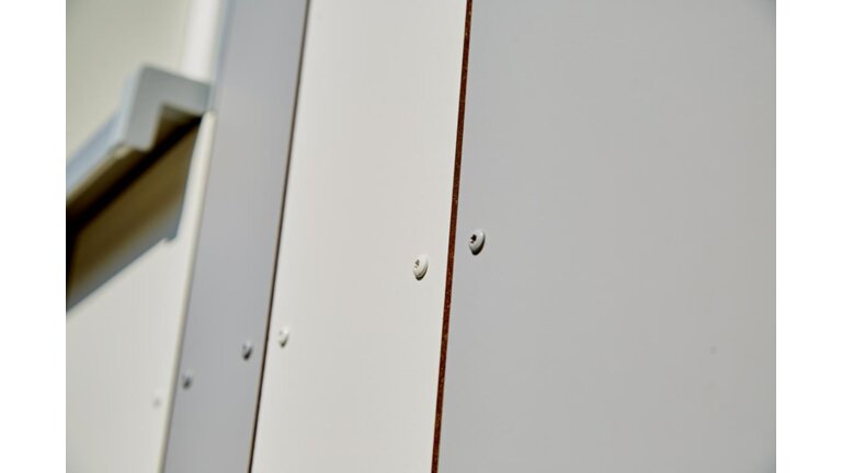 Nahaufnahme einer glatten, weißen Verkleidung mit sichtbaren Befestigungsschrauben für einen schlichten Look.